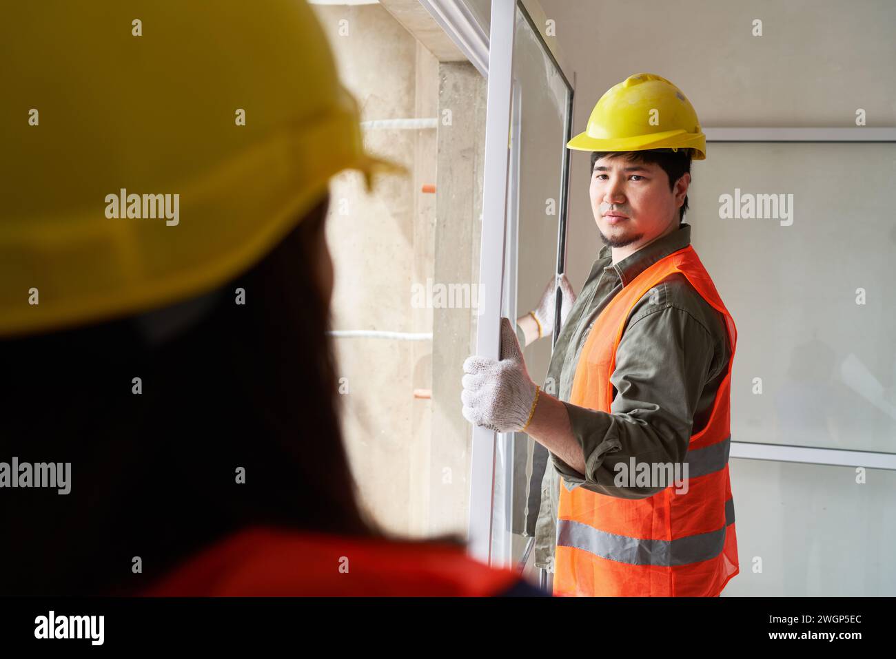 Carpenter carrying window while looking at coworker Stock Photo