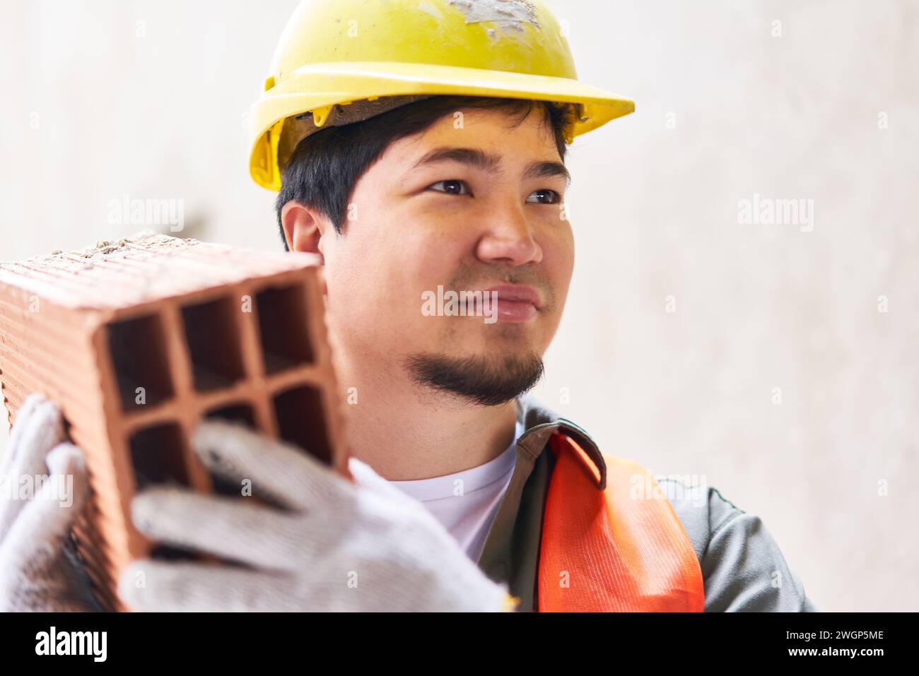 Smiling young male mason carrying brick Stock Photo