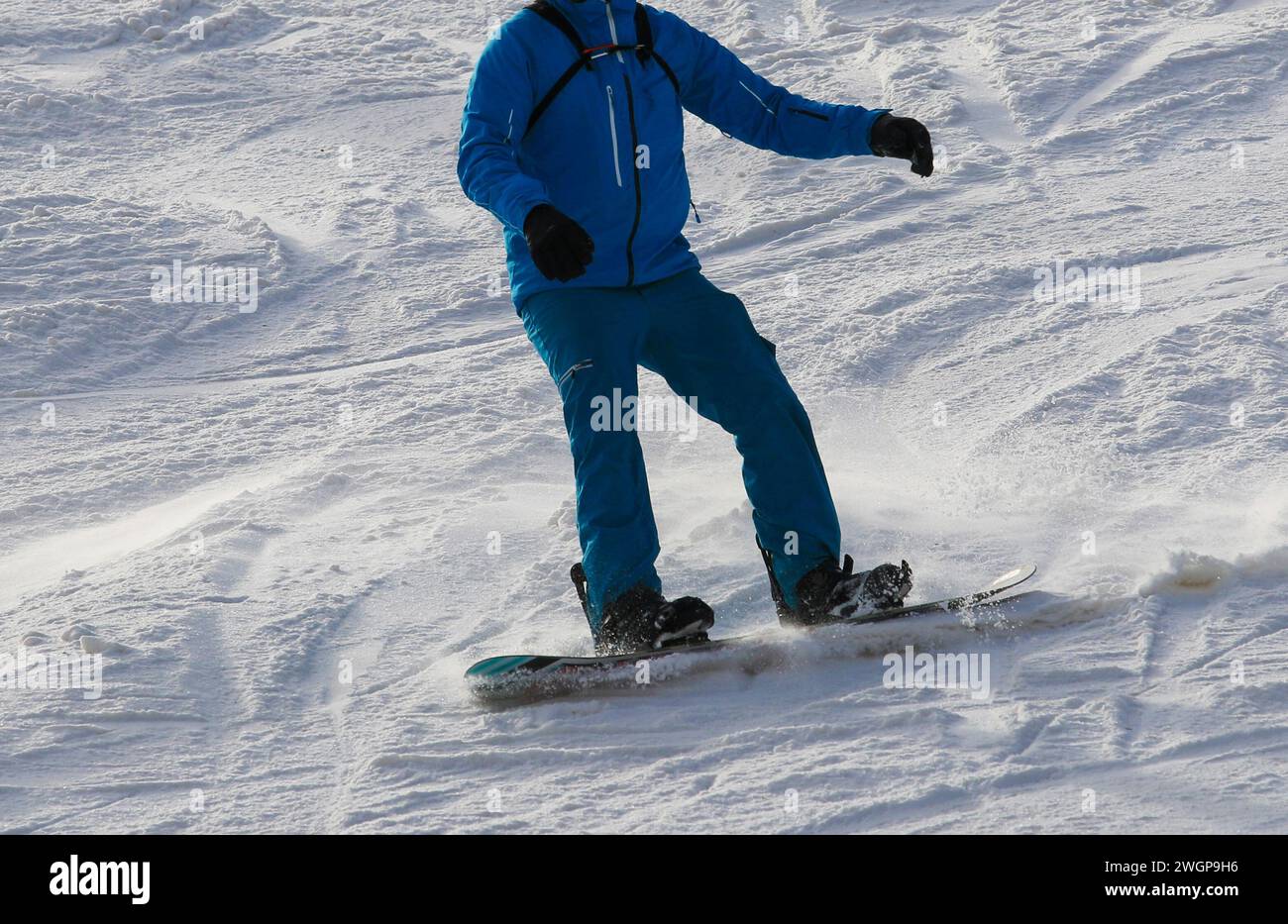 Close up of a snowboarder skiing down a mountain wearing a blue coat and snow pants. Stock Photo