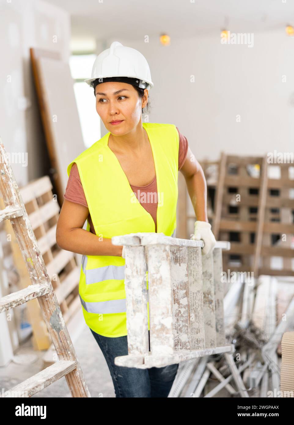 Woman builder carrying stepladder Stock Photo