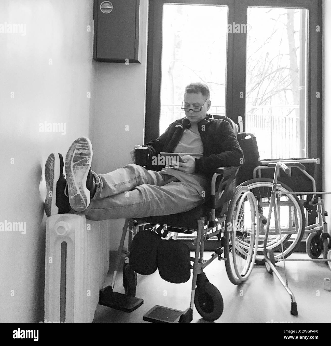 A man sitting in a hospital wheelchair reading a book. Black and white ...
