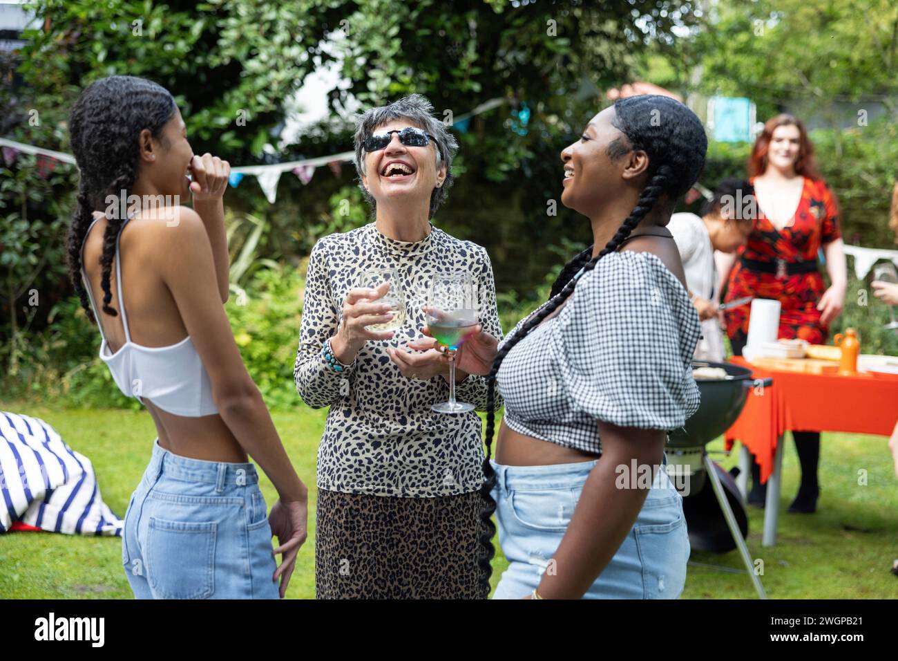 Older woman laughing and having fun with two young women  / grand daughters  /female friends at a summer garden BBQ party. Stock Photo