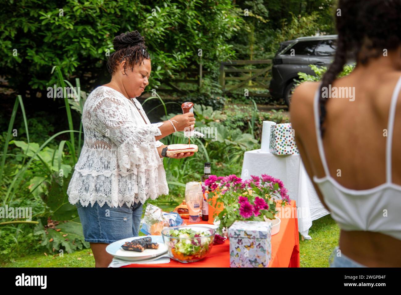 Women enjoying a summer BBQ garden party cooking and eating outside Stock Photo
