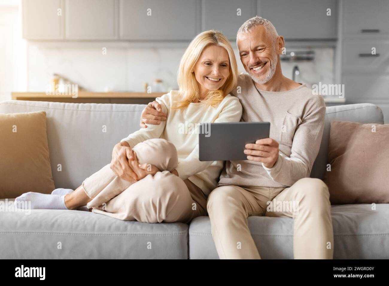 Positive beautiful loving senior spouses using digital tablet at home Stock Photo