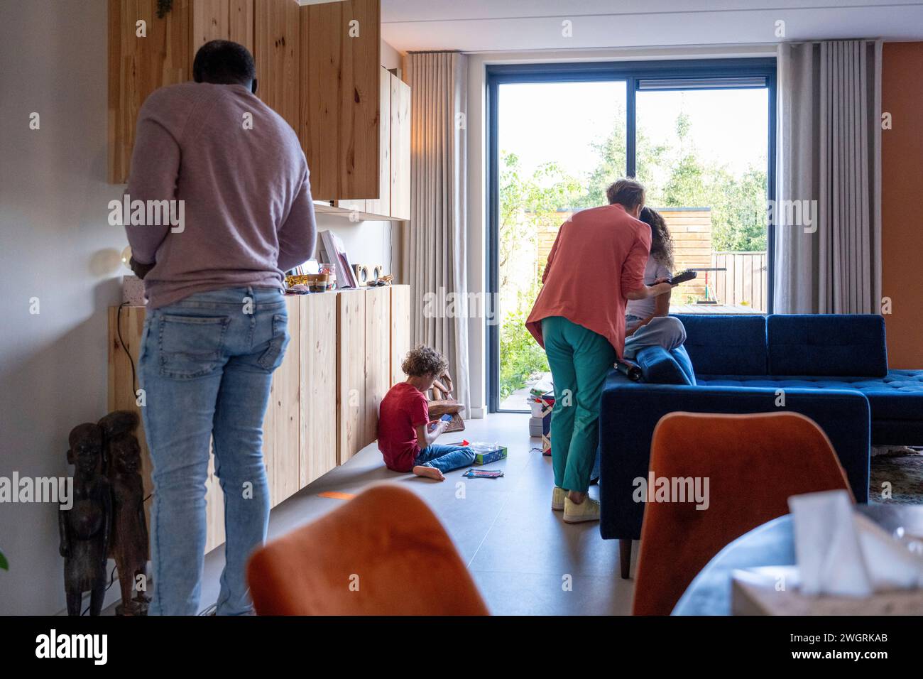 Mixed race family at home, family life, little boy playing on the floor. Dad organising, mum and daughter chatting near the sofa Stock Photo