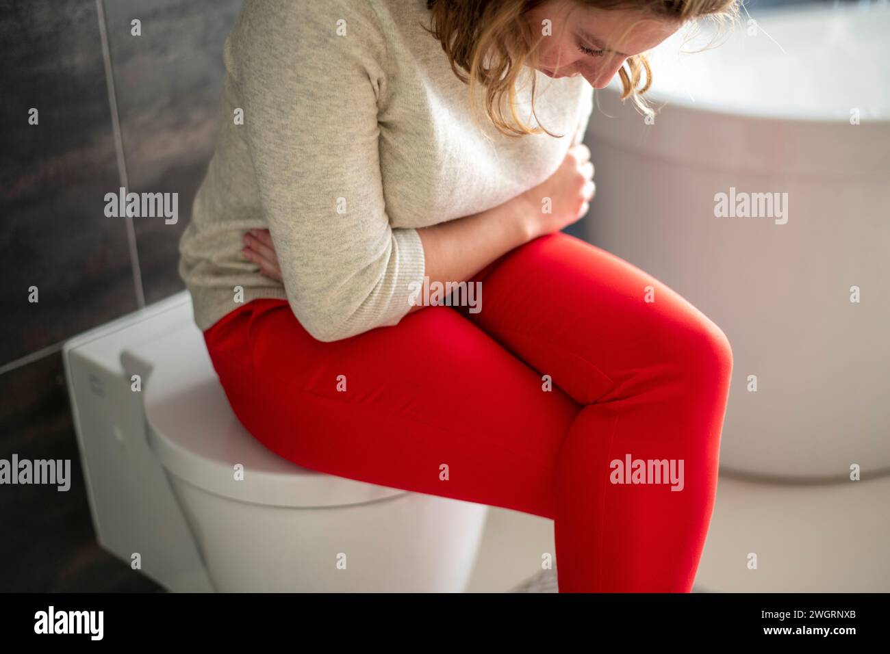 Woman sitting on the toilet with a head ache and cramps from her monthly menstruation period. head in her lap with health pains Stock Photo