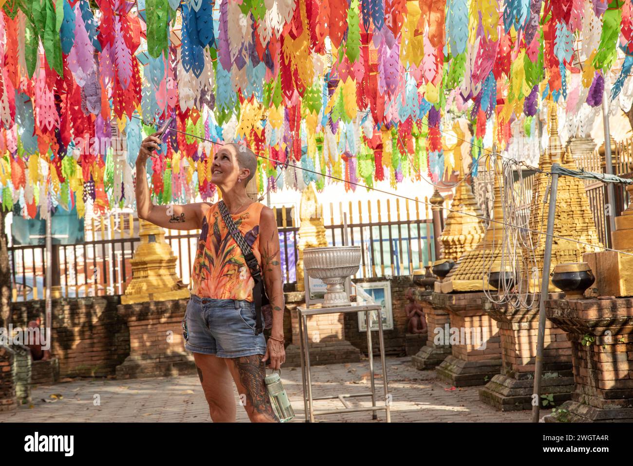 Mid aged woman solo traveller tourist is exploring the Temples in Thailand, she is taking pictures with her phone Stock Photo