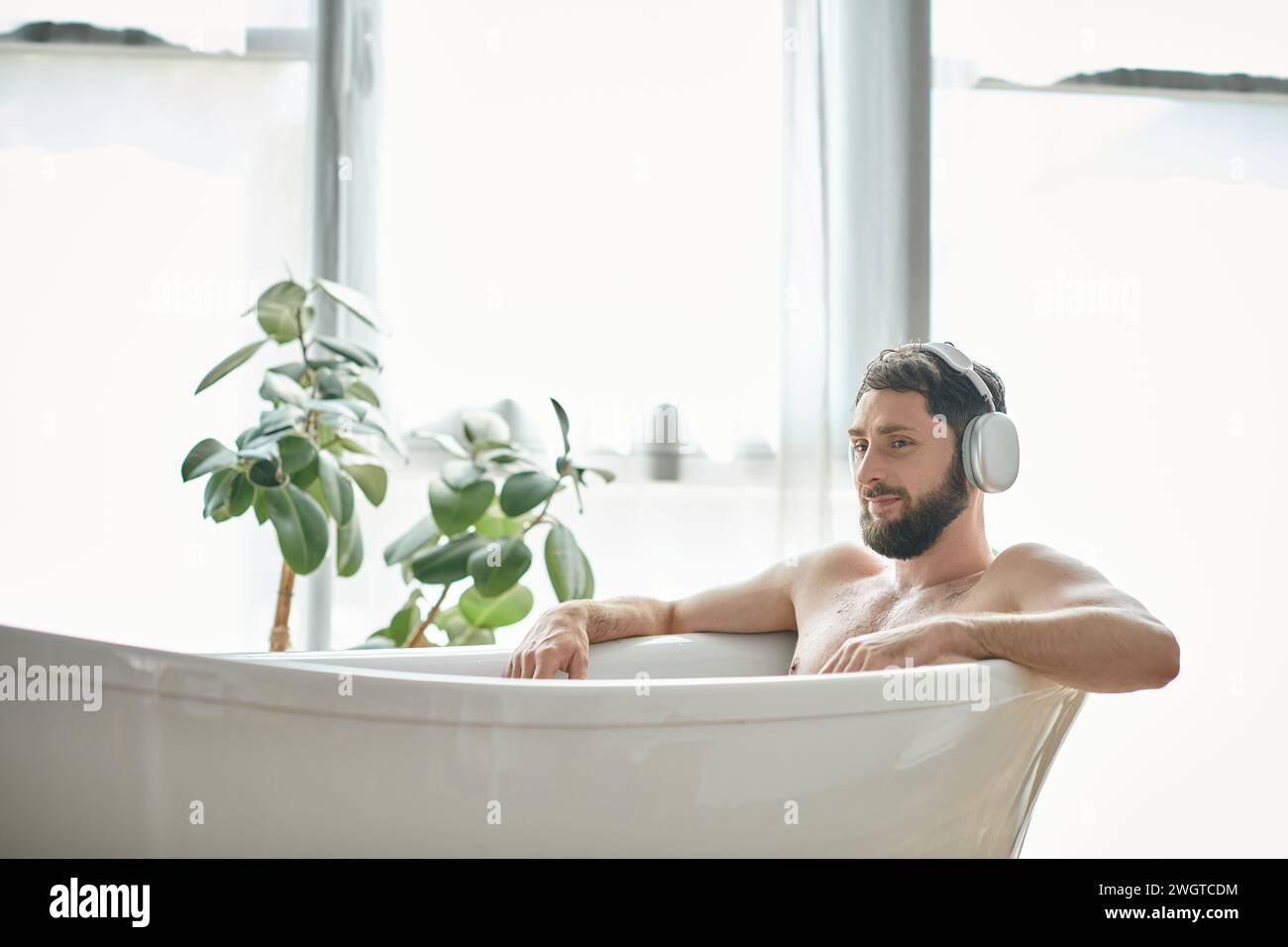 jolly good looking man with beard and headphones sitting and relaxing in his bathtub, mental health Stock Photo