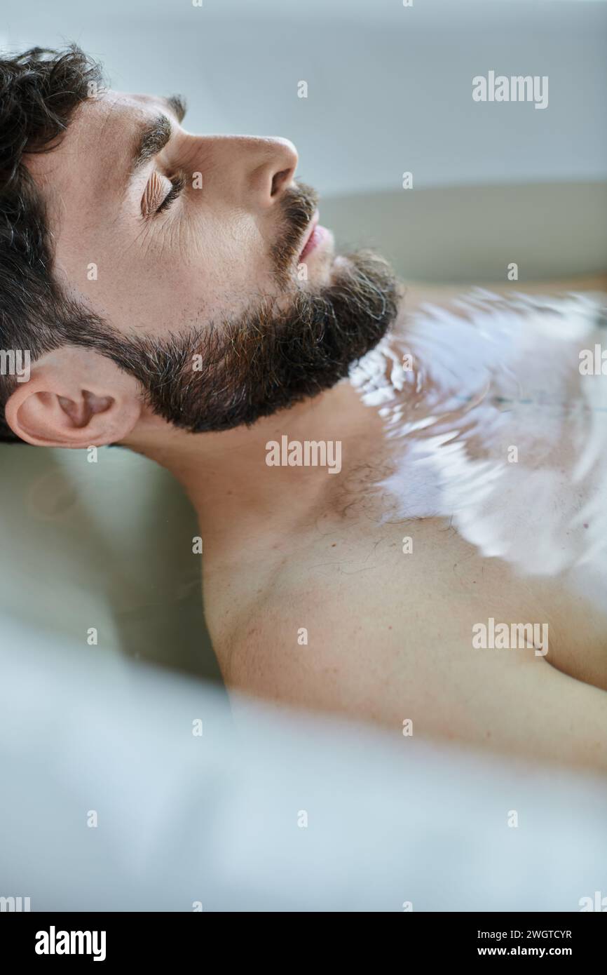 depressed traumatized man with beard lying in bathtub during breakdown, mental health awareness Stock Photo