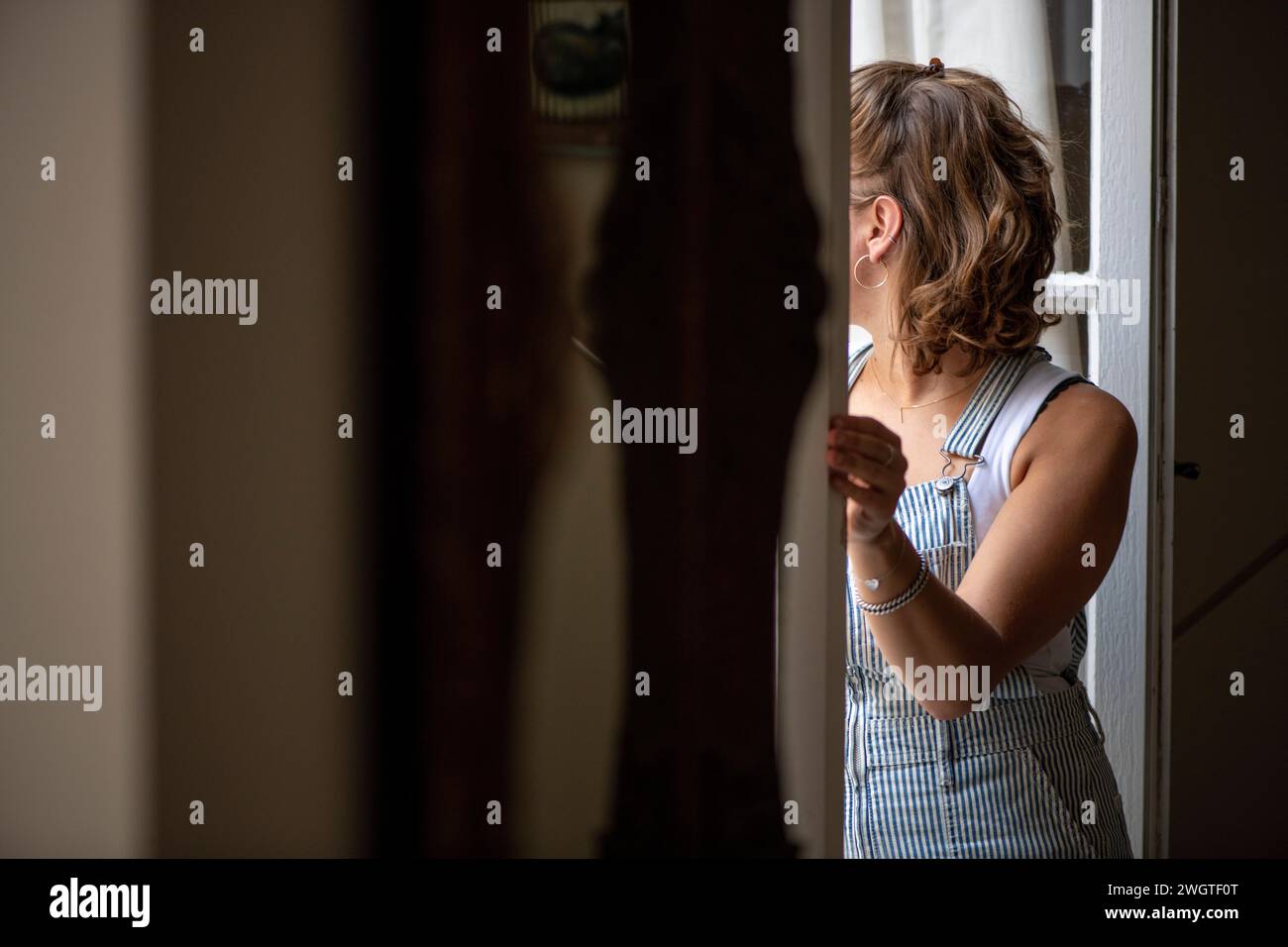 young woman closing the blinds and looking out to the garden from her view Stock Photo