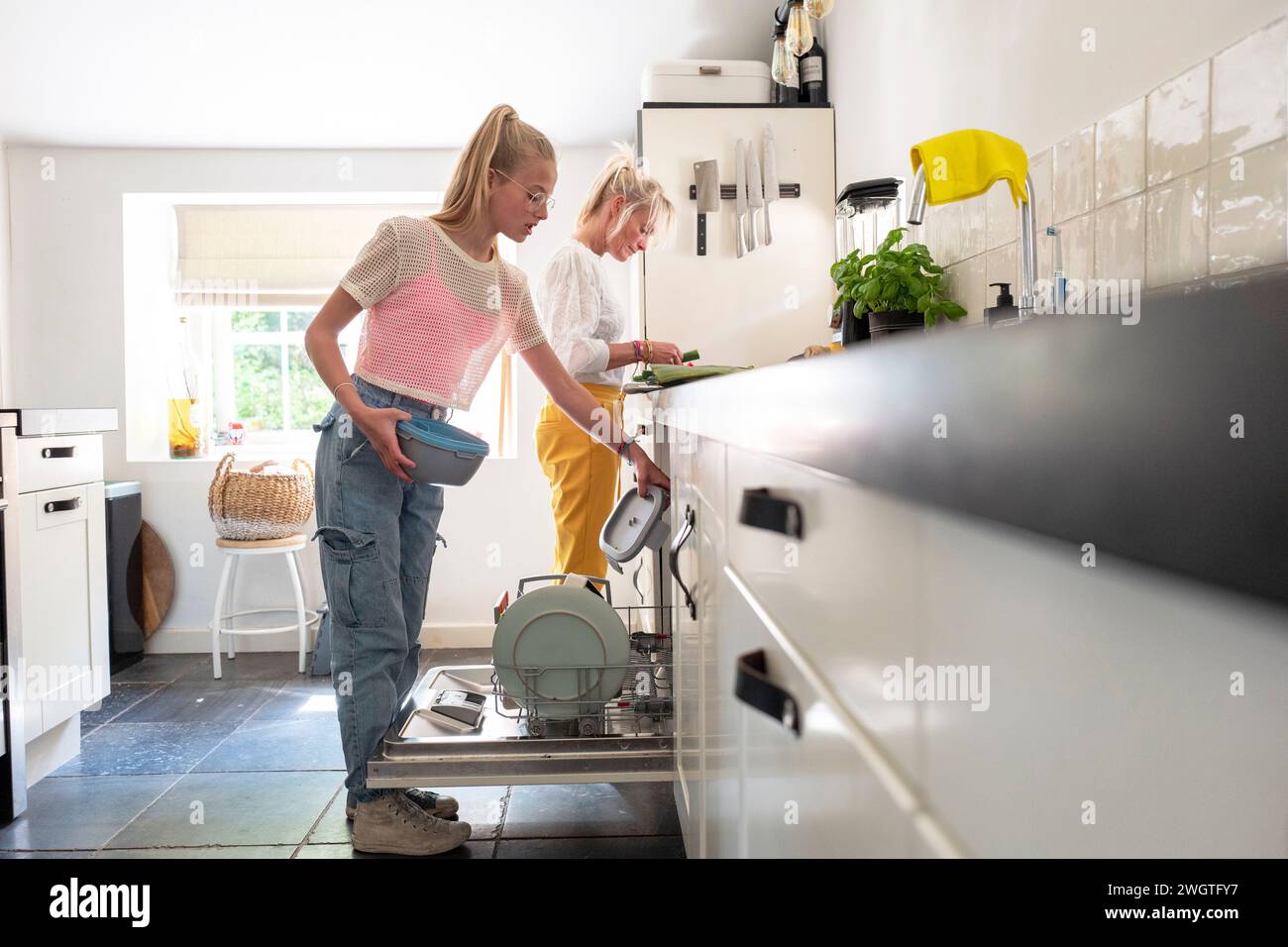 Mother and daughter making and cleaning up diner together in their kitchen. Bright and light with sun coming through the window Stock Photo