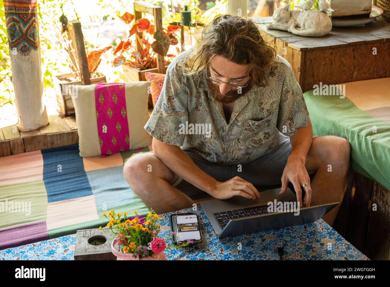Young Man works on his laptop and phone in a restaurant in Northern Thailand, He is a digital Nomad working remotely. Stock Photo