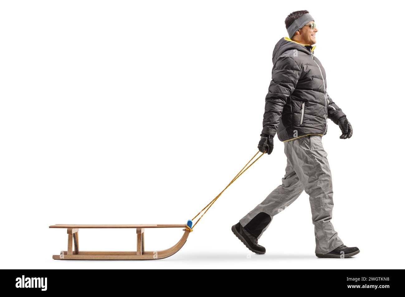 Full length profile shot of a man in a winter jacket walking and pulling a wooden sled isolated on white background Stock Photo