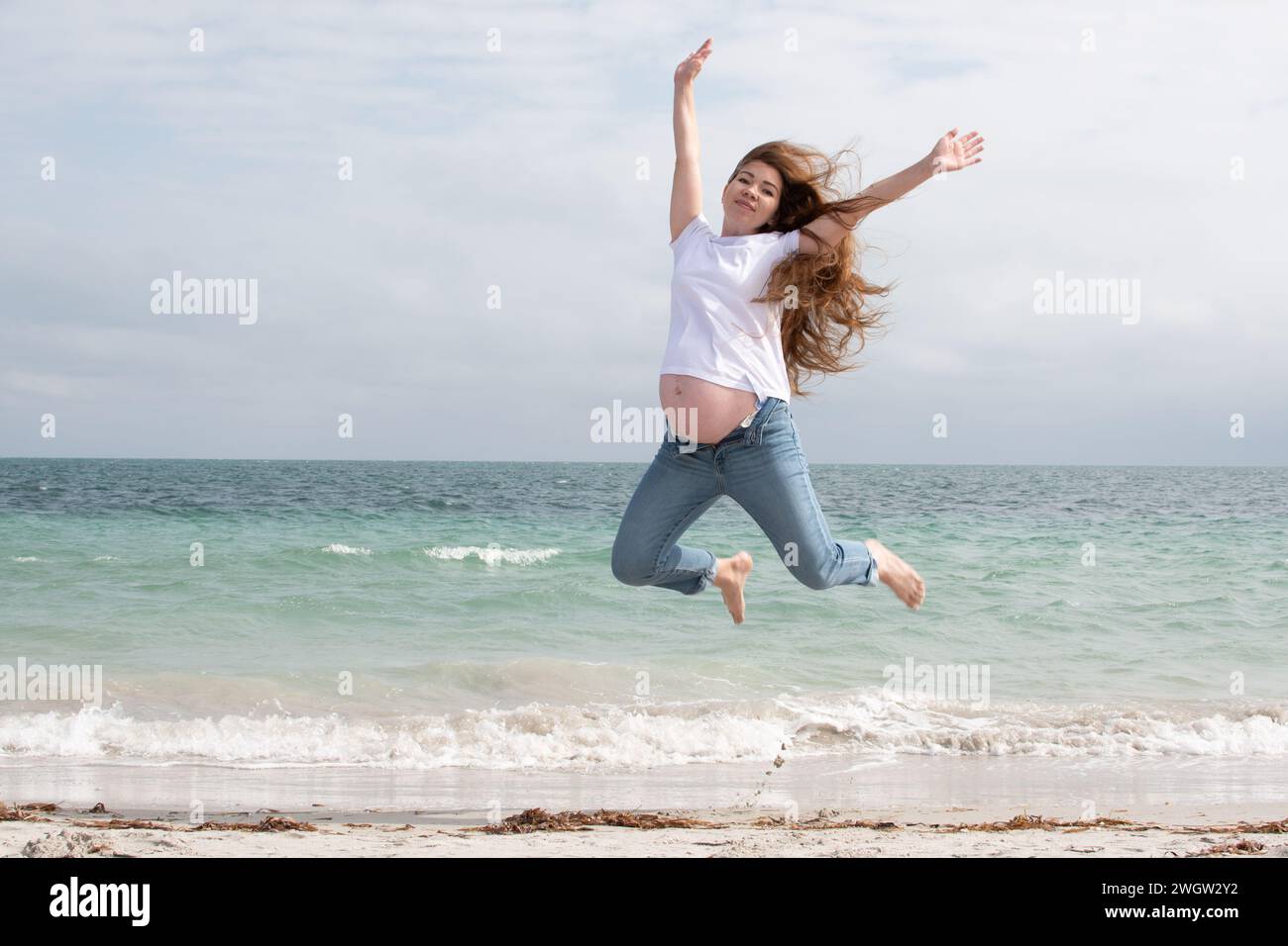 Happy pregnant woman jumps in the air. Happy pregnancy. Active, healthy pregnancy. Pregnant woman near the ocean jumping with glee Stock Photo
