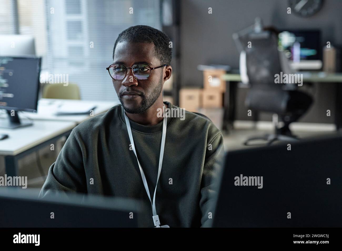 Minimal portrait of focused Black man using computer in IT development office with code lines reflection in glasses copy space Stock Photo