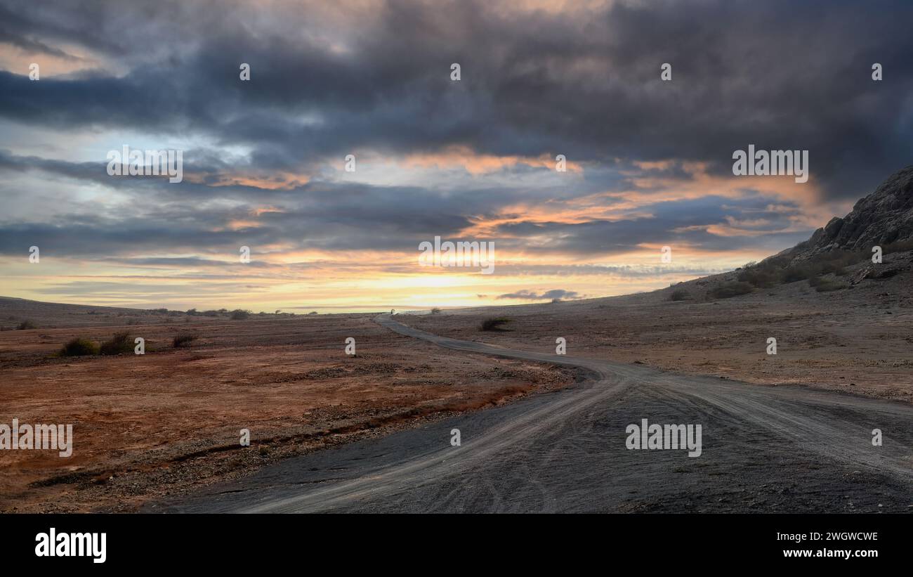The road in Boa Vista's desert leads to mountains under a vibrant sunset sky. High quality photo Stock Photo