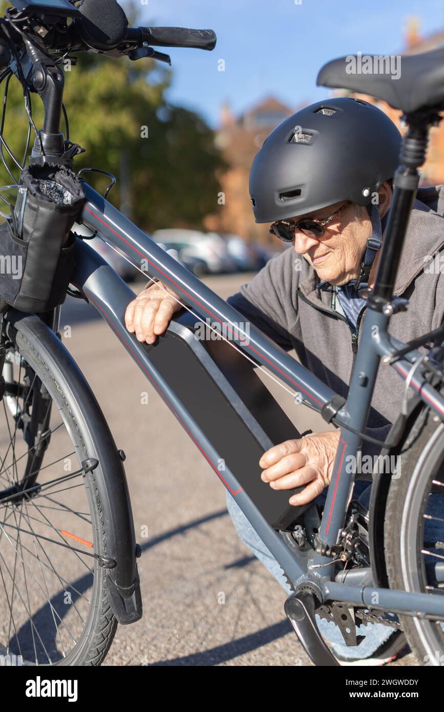 granny cyclist changing battery on e-bike Stock Photo
