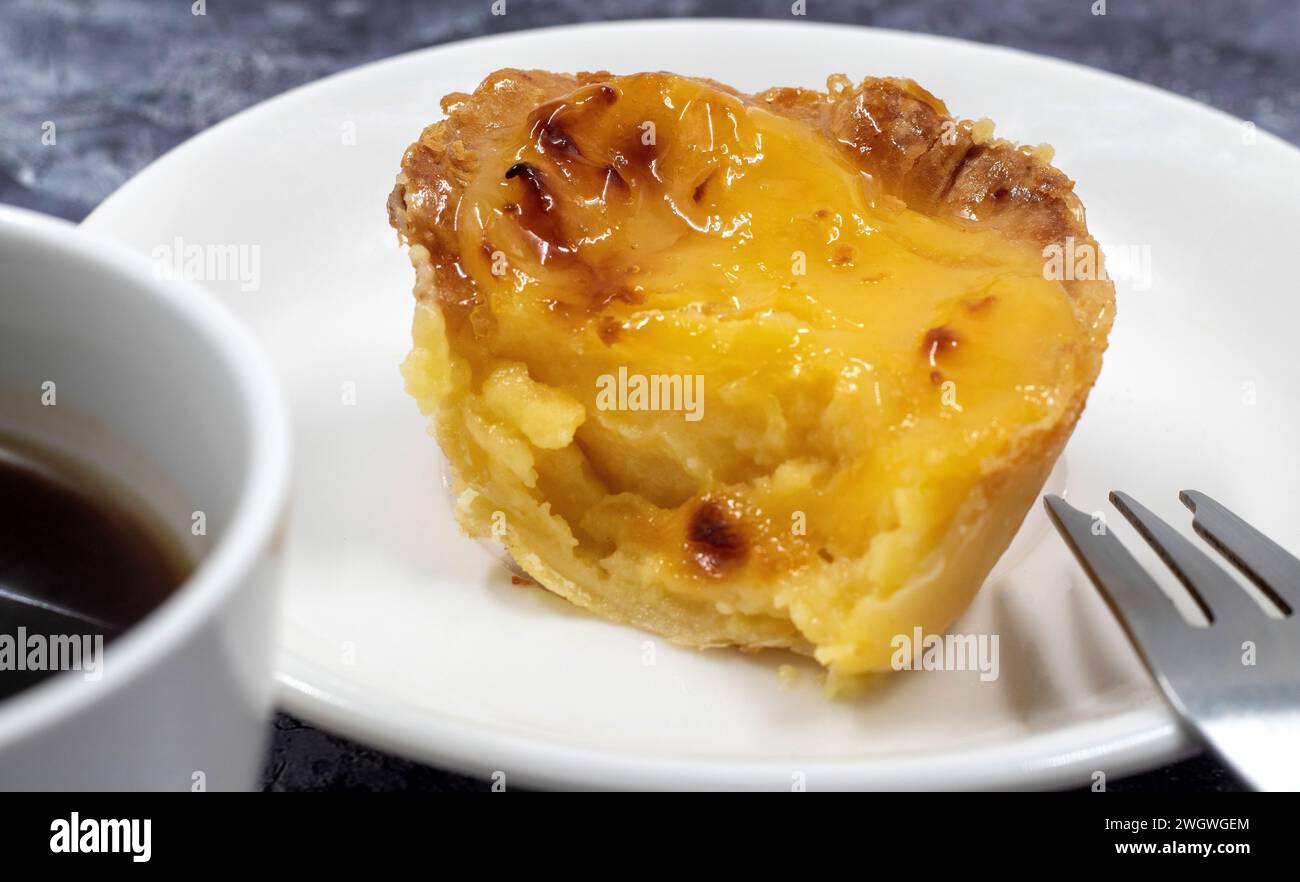 One Pastel de nata or Portuguese egg tart on a white plate. Pastel de Belm is a small pie with a crispy puff pastry crust and a custard cream filling Stock Photo