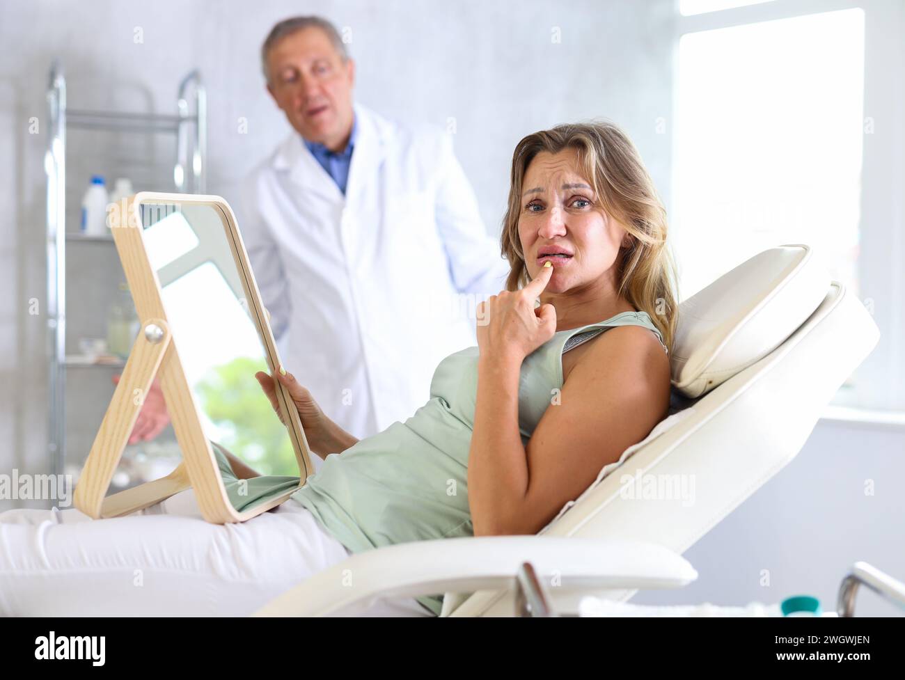 Disappointed woman touching lips after cosmetic treatments in medical office Stock Photo