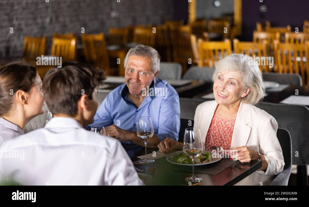 Young family and elderly couple of spouses eating in cafe celebrating event and communicating Stock Photo