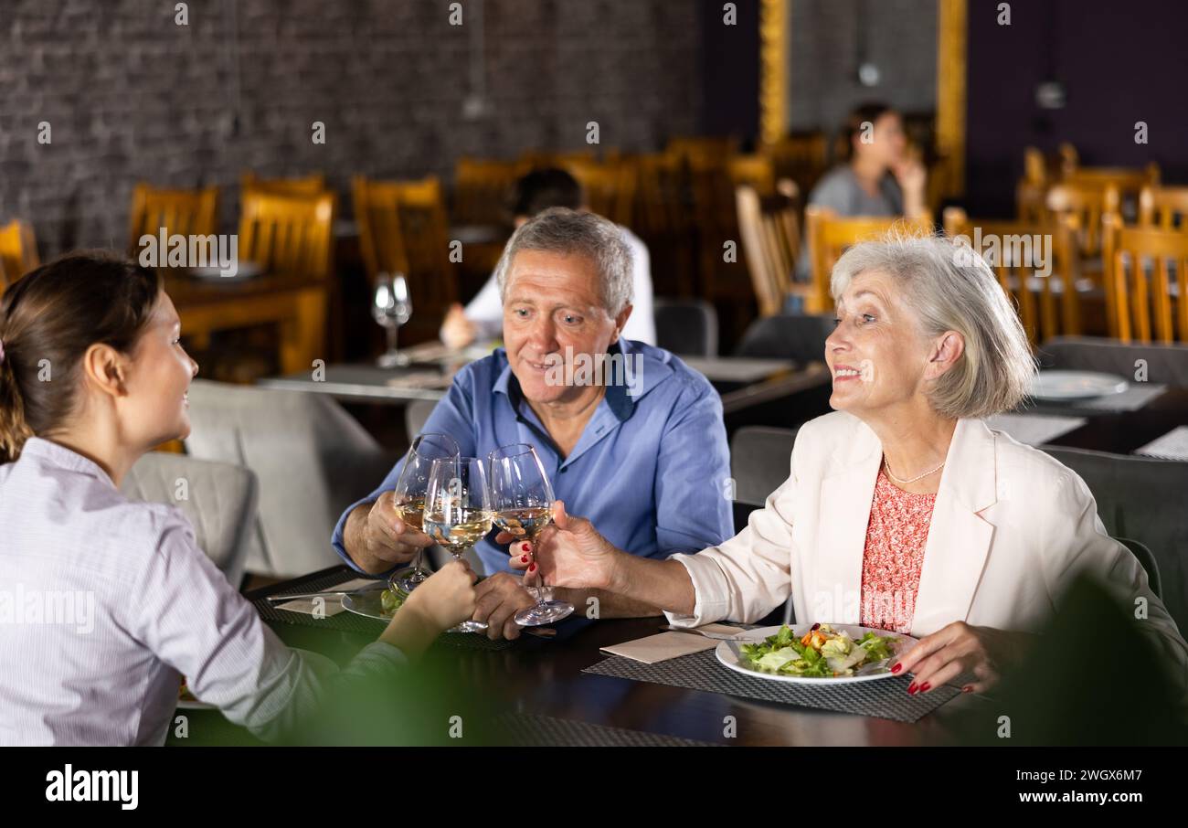 Elderly parents and adult daughter in cafe celebrate family important event occasion. Stock Photo