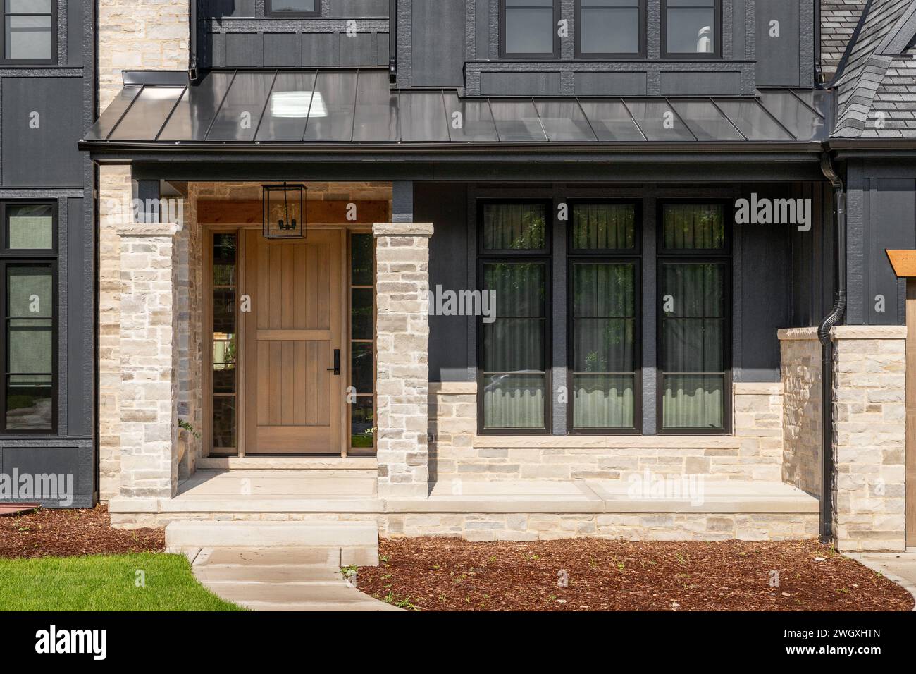 A front door detail on a home with black board and batten siding with natural stone accents and a beautiful oak front door. Stock Photo