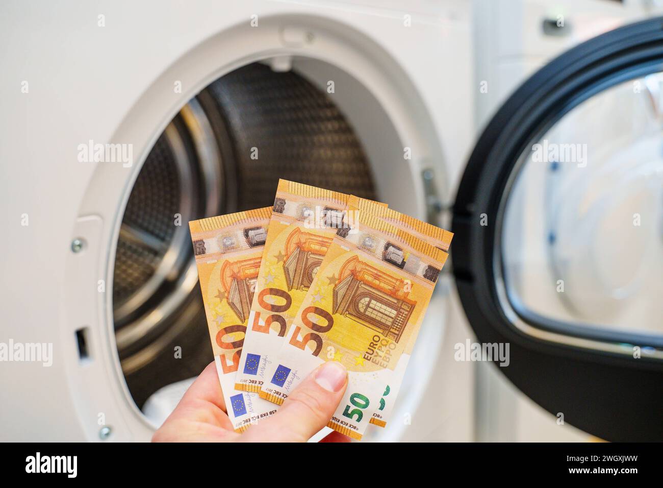 Augsburg, Bavaria, Germany - September 2, 2023: Hand holding 50 euro banknotes in front of a washing machine *** Hand hält 50 Euro Geldscheine vor eine Waschmaschine Stock Photo