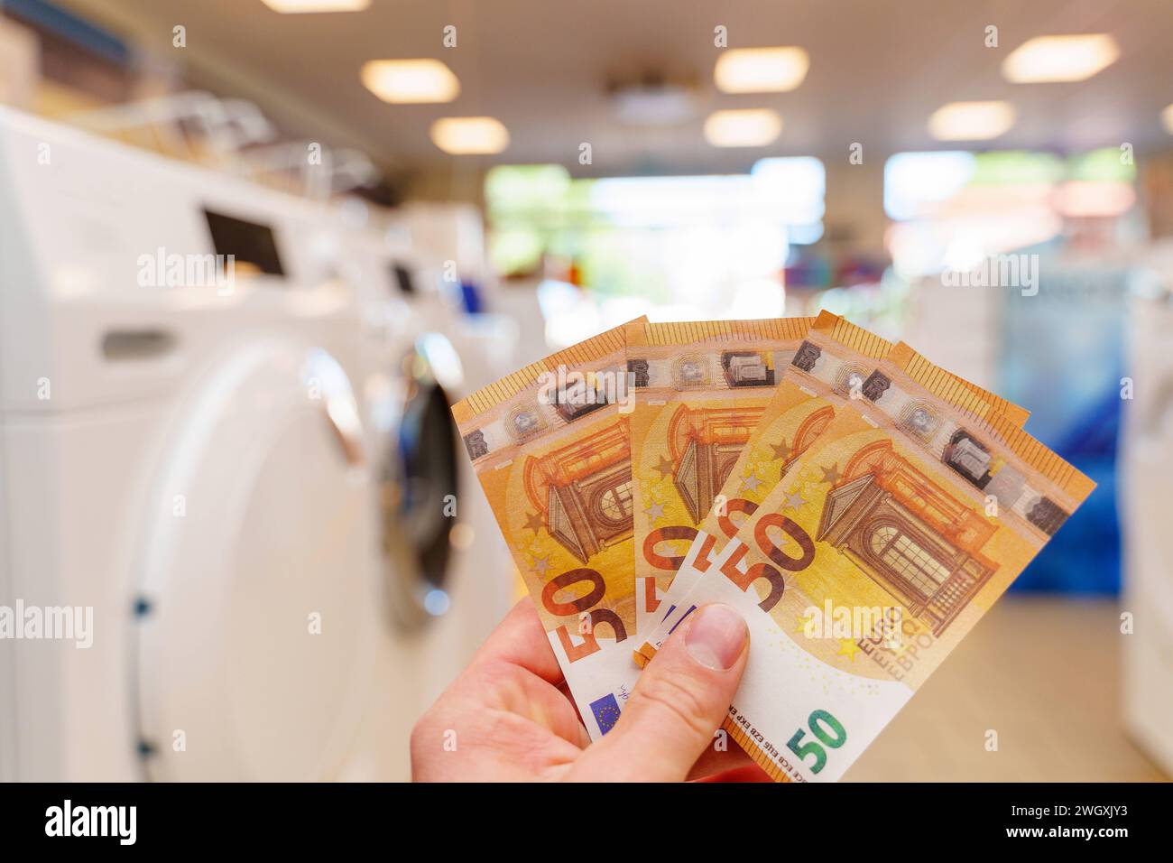 Augsburg, Bavaria, Germany - September 2, 2023: Hand holding 50 euro banknotes in front of a washing machine *** Hand hält 50 Euro Geldscheine vor eine Waschmaschine Stock Photo