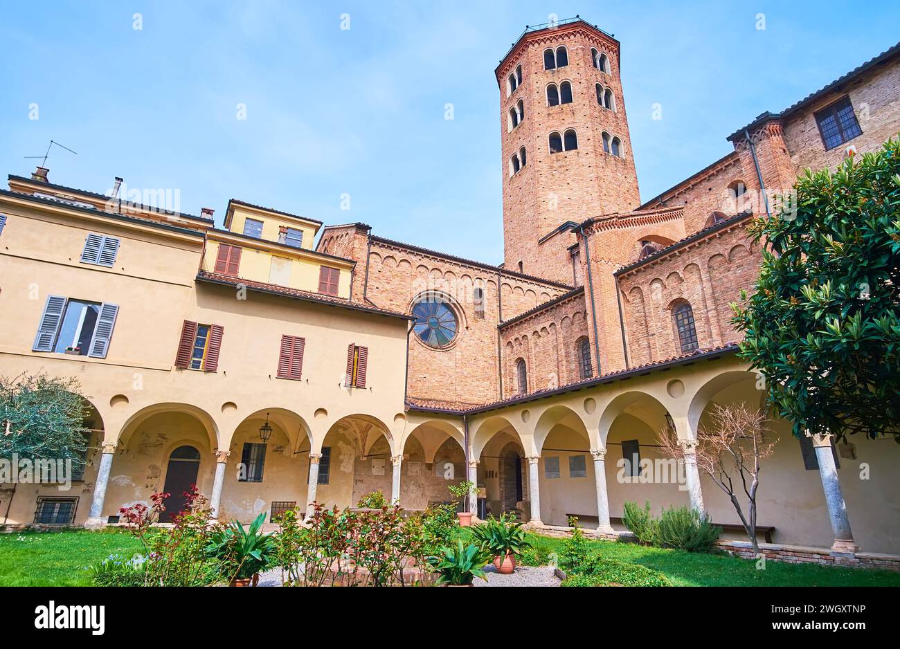 The medieval courtyard of St Antoninus Basilica with a small garden, arched galleries and a campanile (bell tower) of the church, Piacenza, Italy Stock Photo