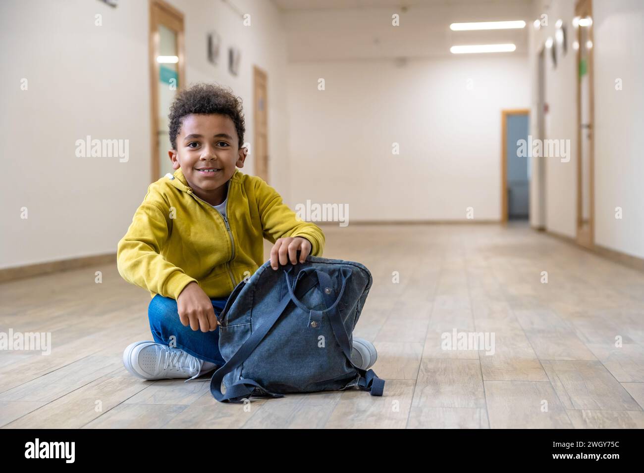 Back to school. Schoolboy with backpacks sitting on floor in school corridor during recess. Stock Photo