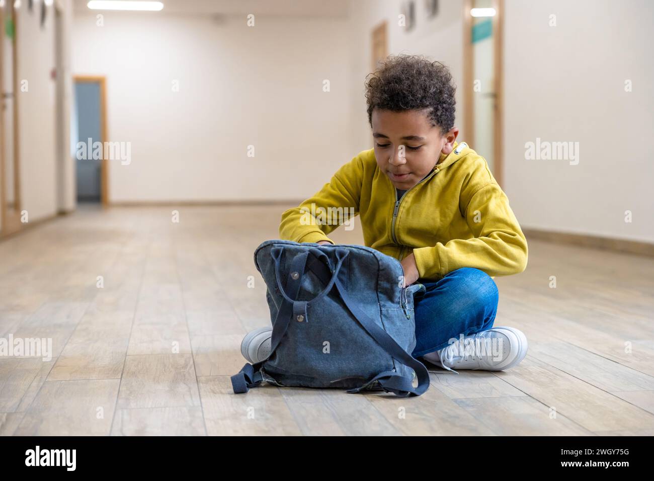 Back to school. Schoolboy with backpacks sitting on floor in school corridor during recess. Stock Photo