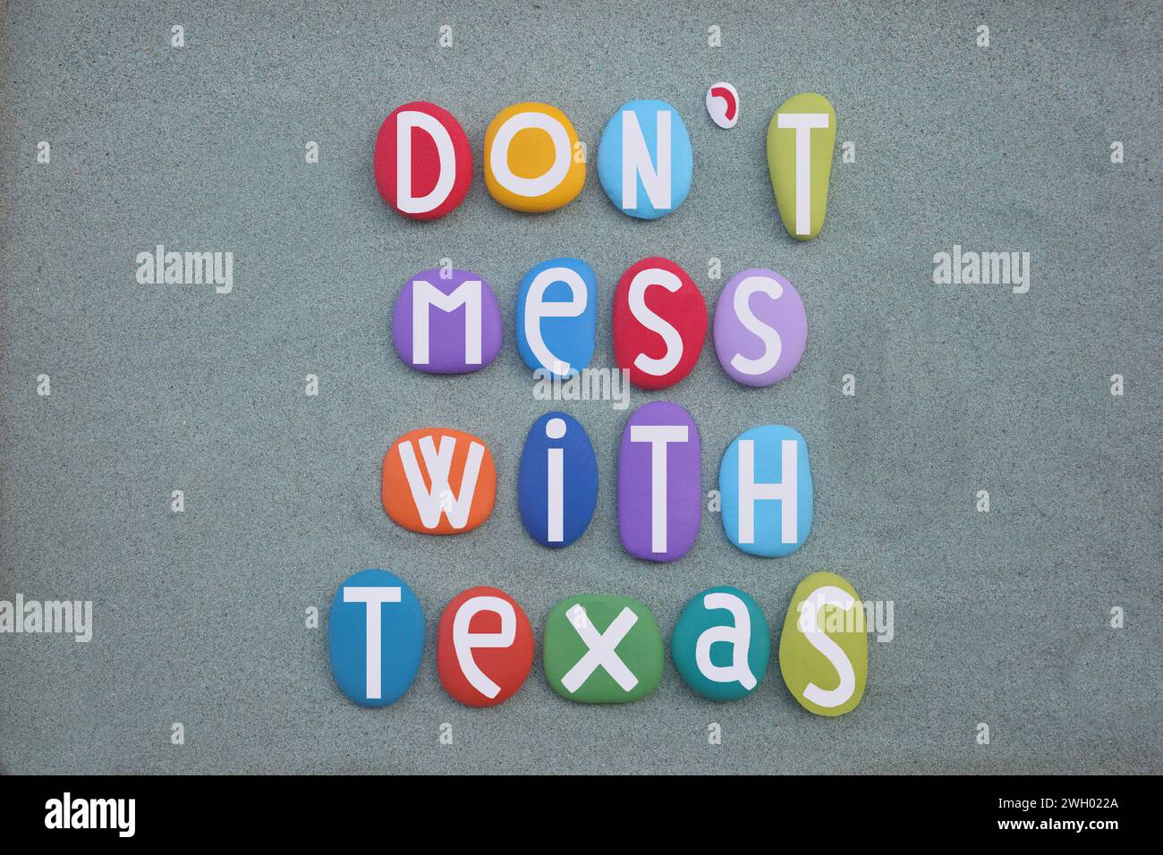 Don't mess with Texas, creative slogan composed with hand painted multi colored stone letters over green sand Stock Photo