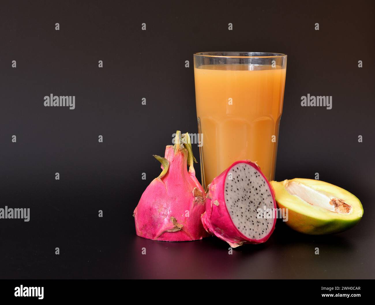 A tall glass of mango juice with pitaya and pieces of ripe fruit on a black background. Close-up. Stock Photo