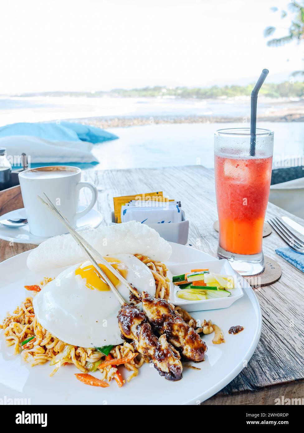 Mie goreng (fried noodles) served with two sticks of chicken satay and a fried egg at a restaurant on the Medewi Beach in Bali, Indonesia. Stock Photo