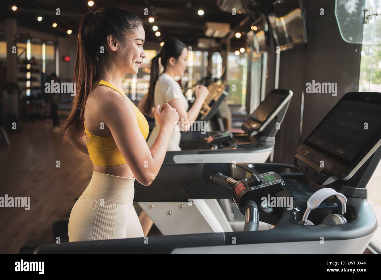 Two young woman are jogging on treadmill during her sports training in a gym. Stock Photo
