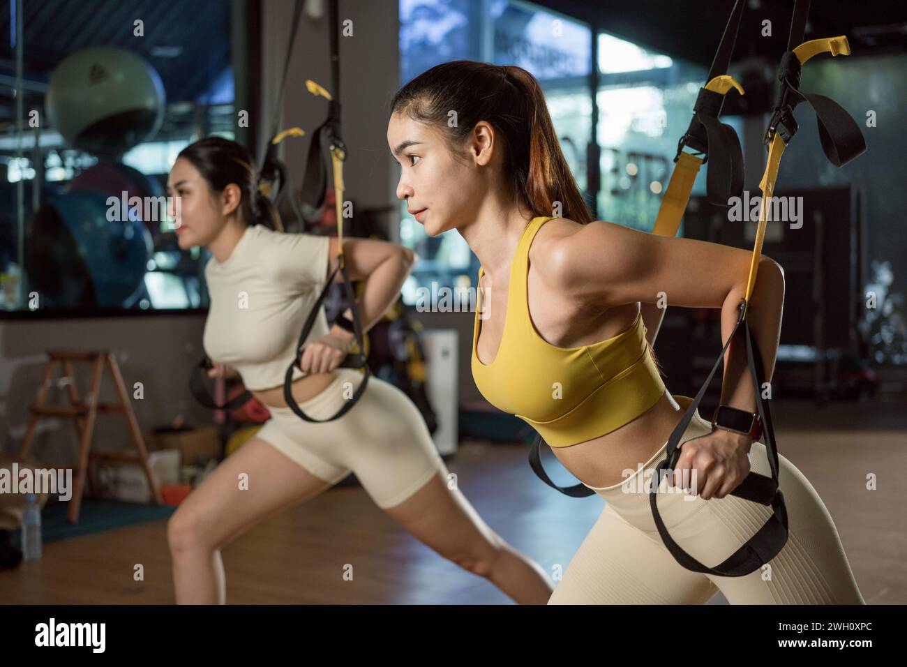 Asian woman doing push ups, arm training with trx fitness straps in the gym. Stock Photo