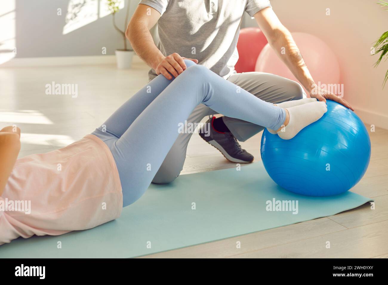 Nurse man helping fat patient woman to do stretching exercises with rubber band sitting on fit ball Stock Photo