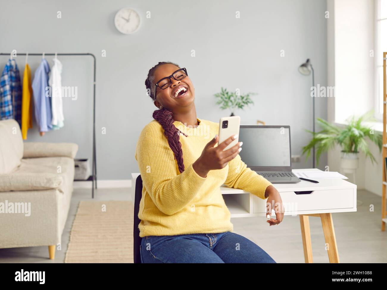 Happy woman working at home, having break, holding phone and laughing at joke on social media Stock Photo