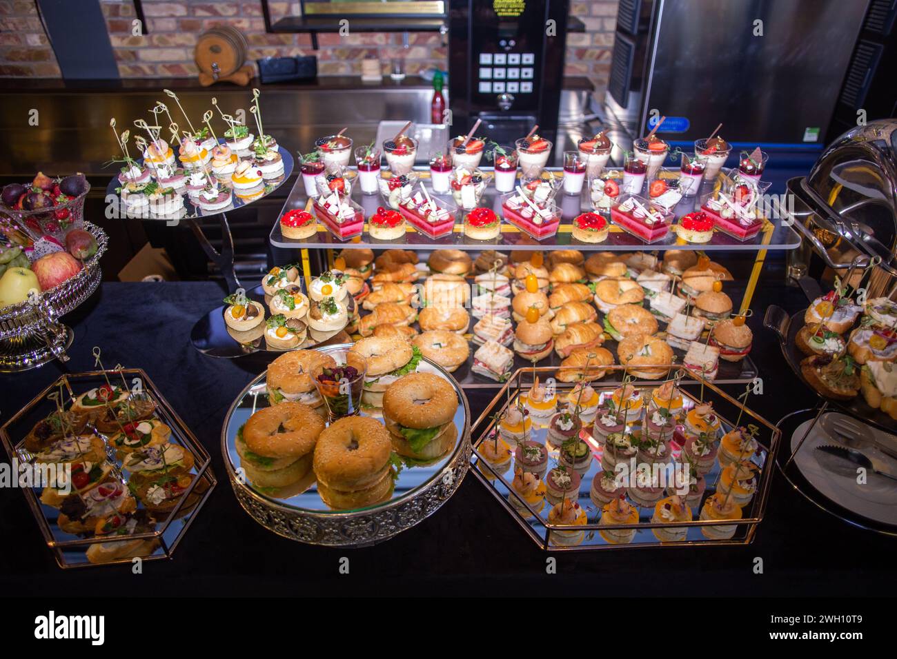 A beautifully presented catering buffet with an array of tempting snacks and desserts. Includes sandwiches, mini burgers, pastries, and fruit, elegant Stock Photo