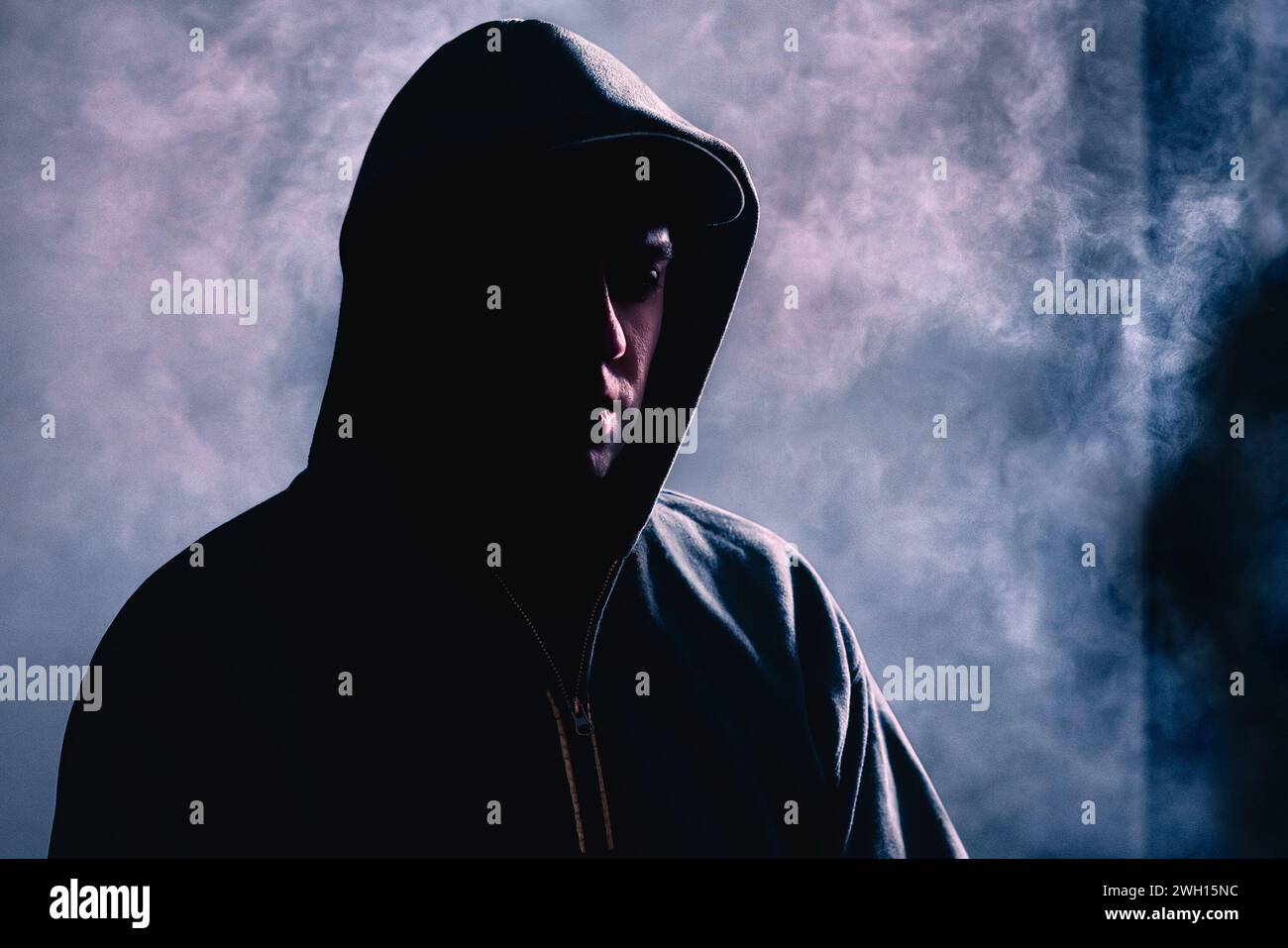 Criminal man in shadow. Scary suspicious stranger with hidden face. Silhouette of gangster with dark smoke fog background. Gang crime or horror. Stock Photo
