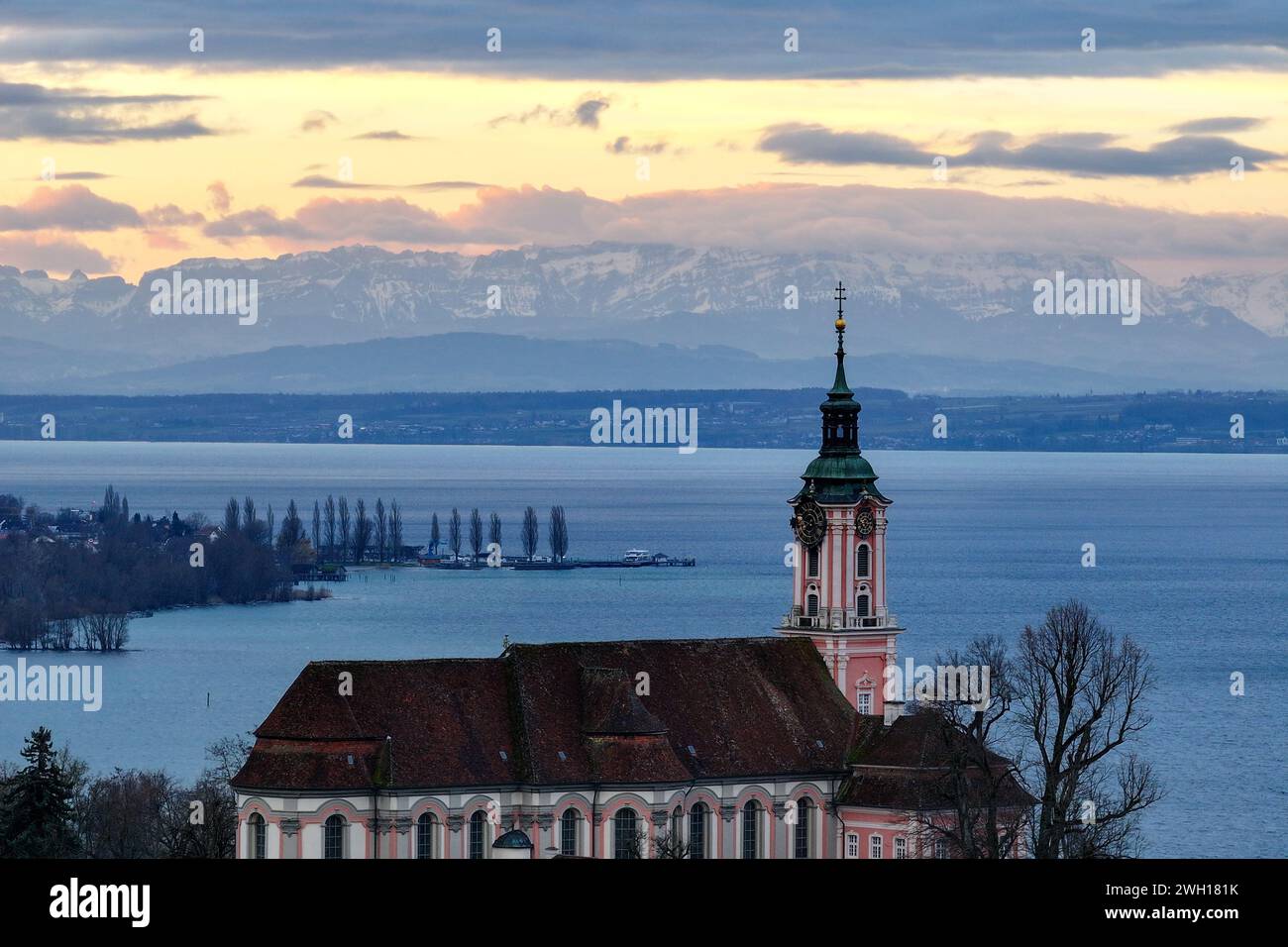 Unteruhldingen Am Bodensee, Germany. 07th Feb, 2024. The sun rises behind the former monastery church of Birnau on Lake Constance. The Alps can be seen in the background. Windy, rainy, but mild: the weather will be rather uncomfortable over the next few days. The German Weather Service has predicted continuous rain for central Germany until Friday. In the eastern low mountain ranges, the precipitation may also turn to snow at times. Shot with a drone Credit: Felix Kästle/dpa/Alamy Live News Stock Photo