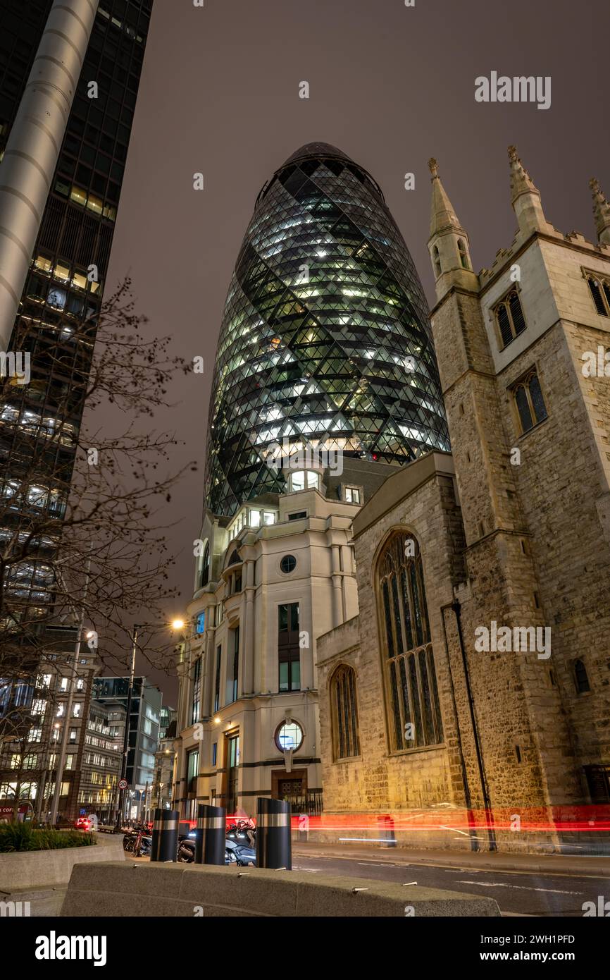 London. UK-02.02.2024. A night time street view of The Gherkin building in the City of London with St. Andrew Undershaft Church in front. Stock Photo