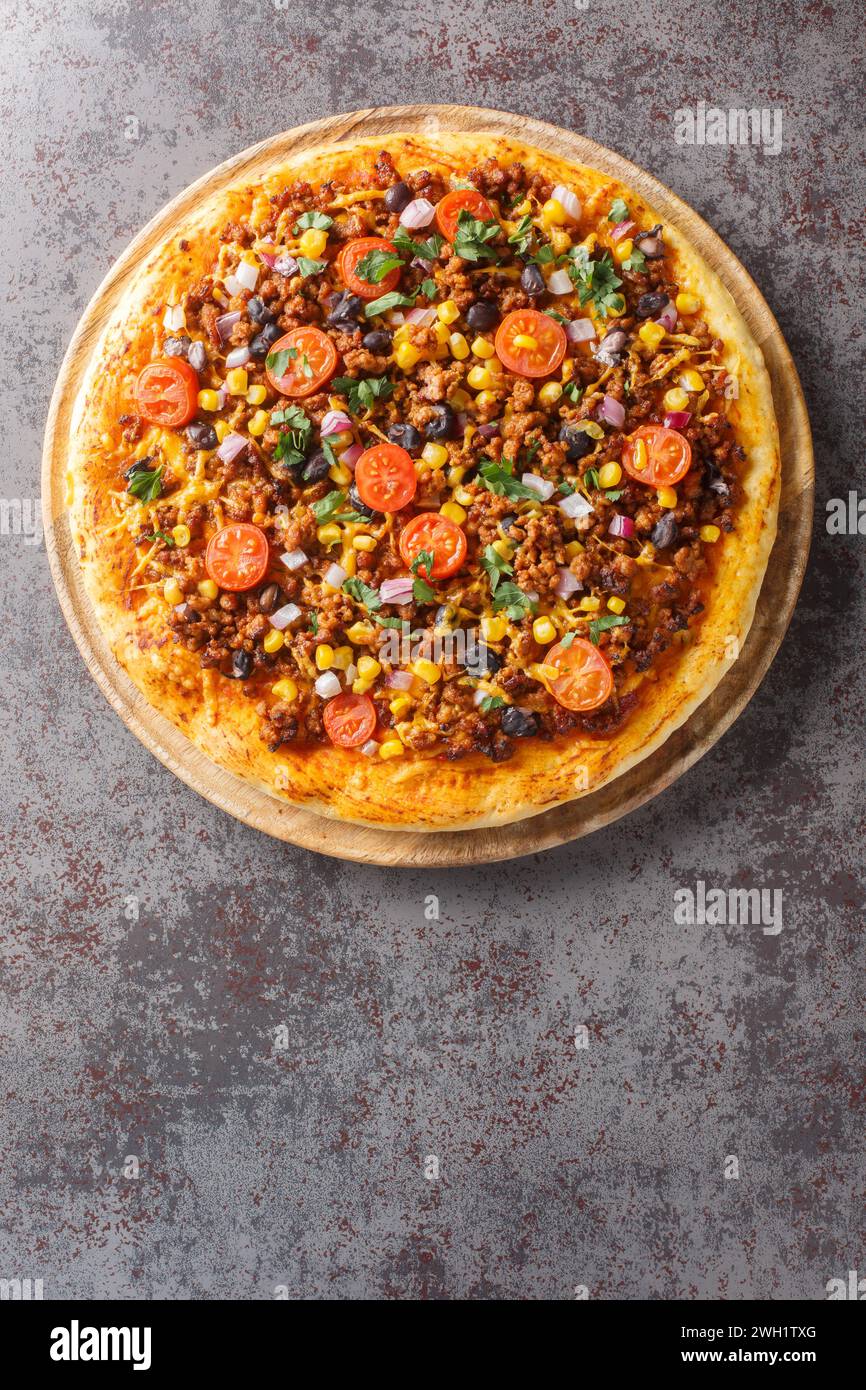 Homemade Spicy Mexican Taco PIzza with ground beef, tomatoes, corn, black beans, cheddar cheese, red onion on the wooden board on the table. Vertical Stock Photo