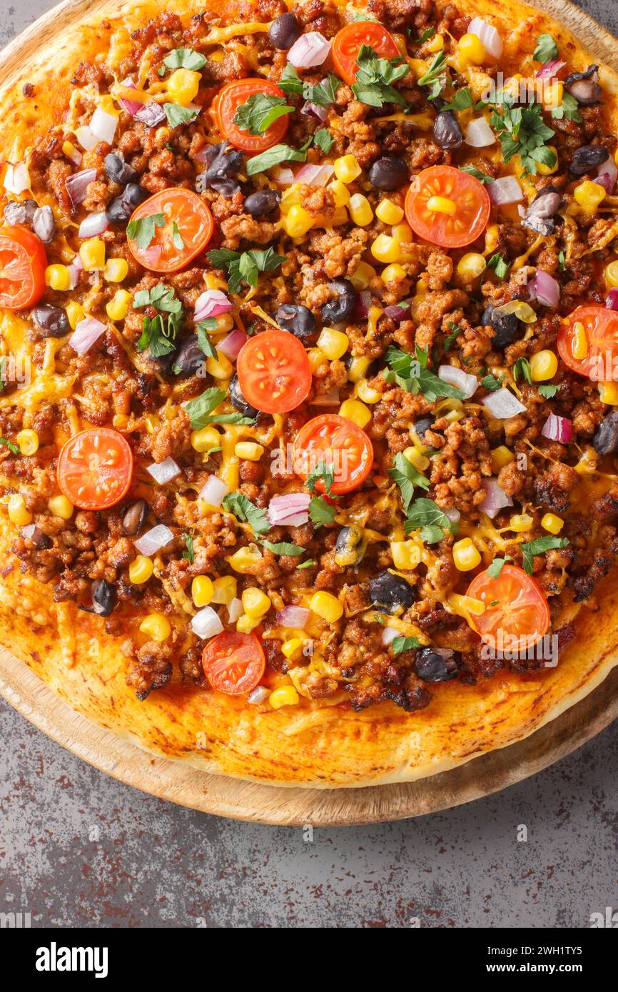 Tex Mex food Mexican American pizza with ground beef, vegetables, cheddar cheese close up on a wooden board on the table. Vertical top view from above Stock Photo