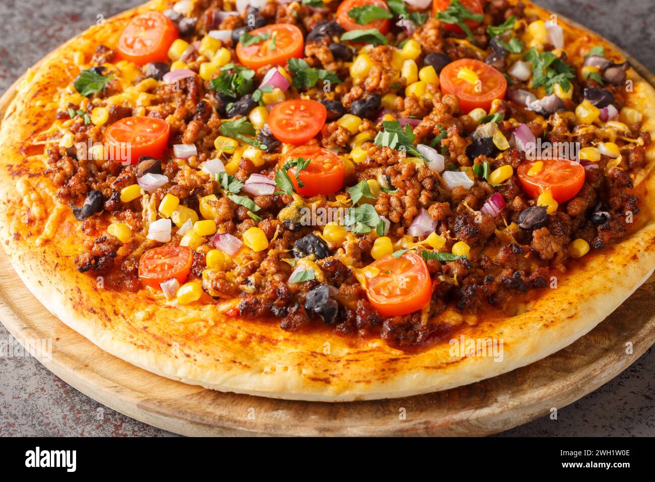 Hot Tex Mex taco pizza with ground beef, salsa, cheddar cheese and Mexican spices close-up on a wooden board on the table. Horizontal Stock Photo