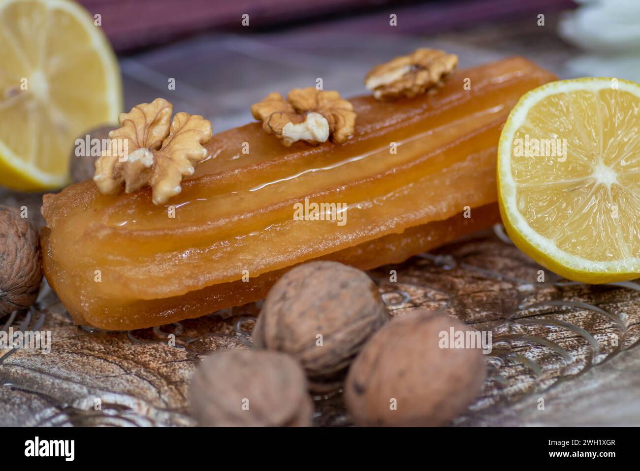 Turkish sweet cake called tulumba, served at plate with sliced of lemon and nuts around, on massive wooden table Stock Photo