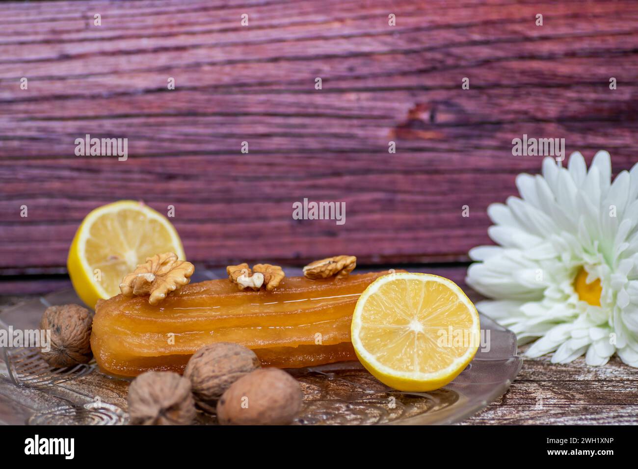 Turkish sweet cake called tulumba, served at plate with sliced of lemon and nuts around, on massive wooden table Stock Photo