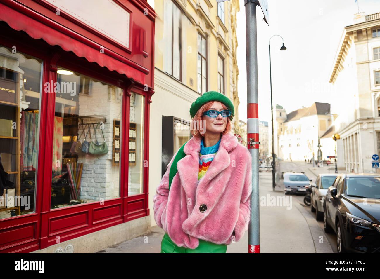 stylish woman in faux fur jacket and sunglasses looking away on urban ...