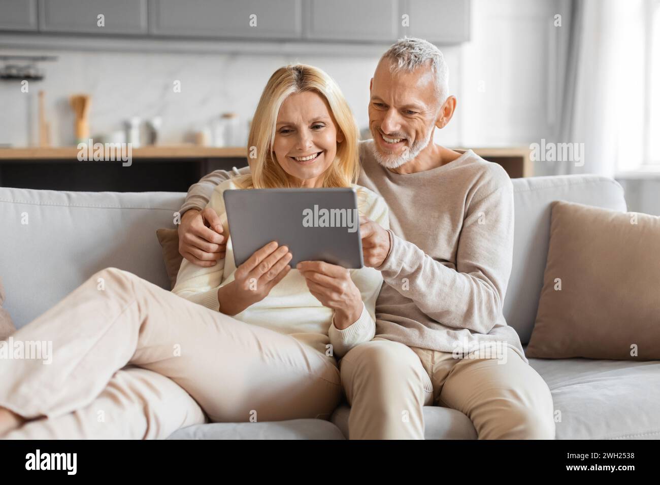 Excited smiling senior spouses using digital tablet computer at home Stock Photo