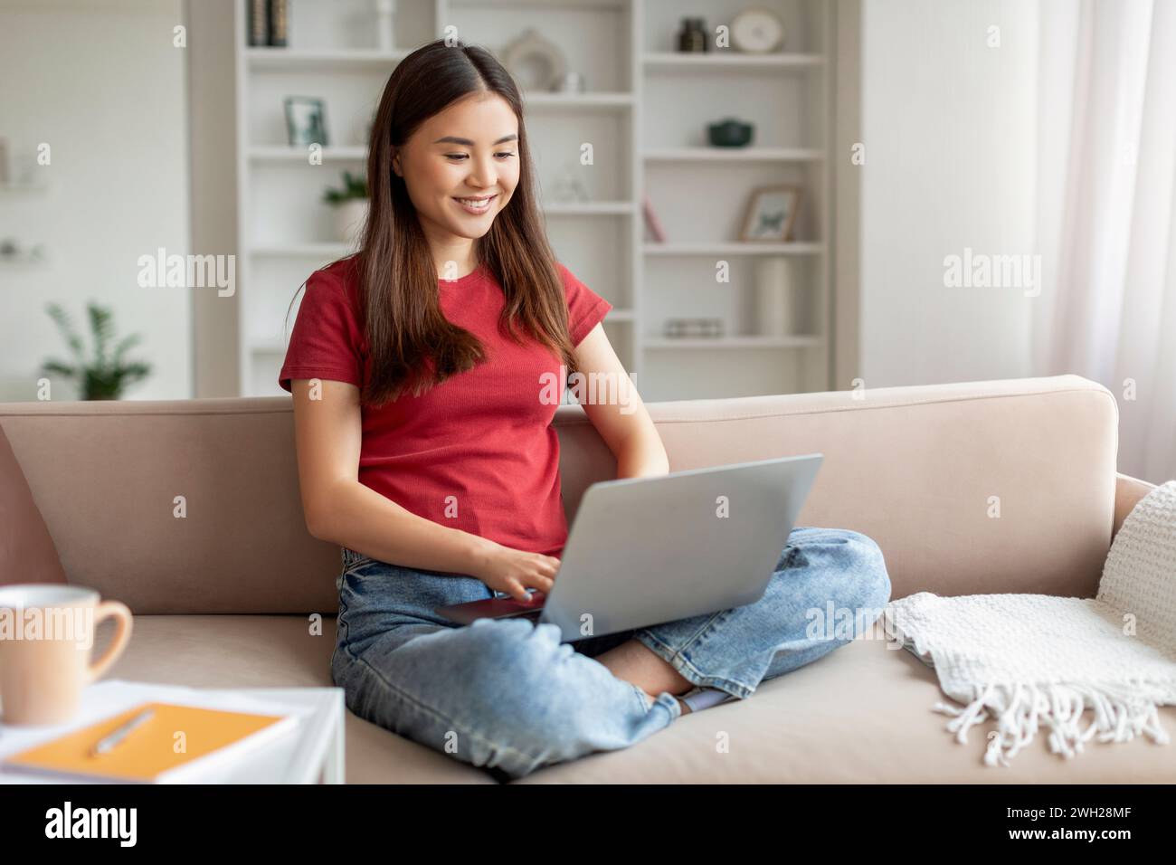 Relaxed young asian woman smiling while browsing on her laptop Stock Photo